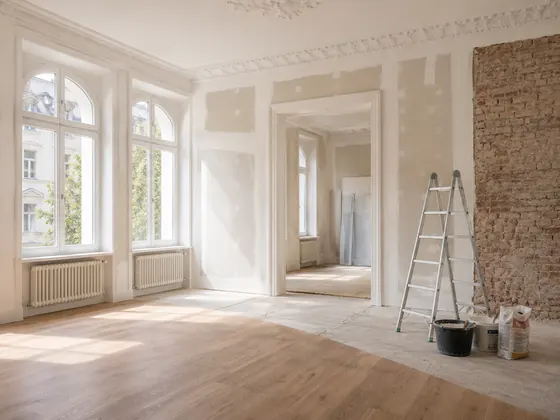 Altbausanierung in einem hellen Raum mit Stuckdecke, freigelegter Ziegelwand und vorbereiteten Renovierungsarbeiten