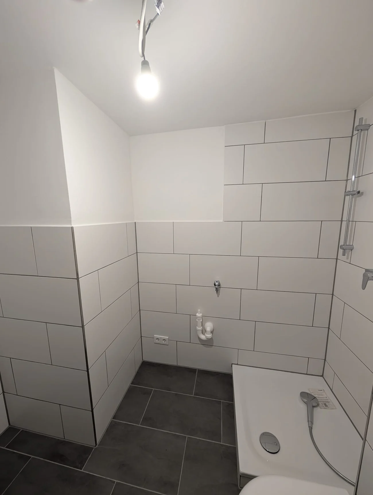 Badezimmer nach der Badsanierung mit neuen Wandfliesen, dunklem Boden und sauber vorbereiteten Anschlüssen