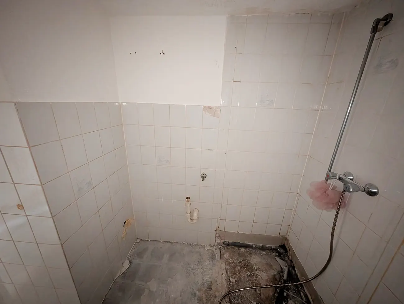 Badezimmer vor der Badsanierung mit alten Wandfliesen, entfernten Sanitärobjekten und vorbereiteter Dusche