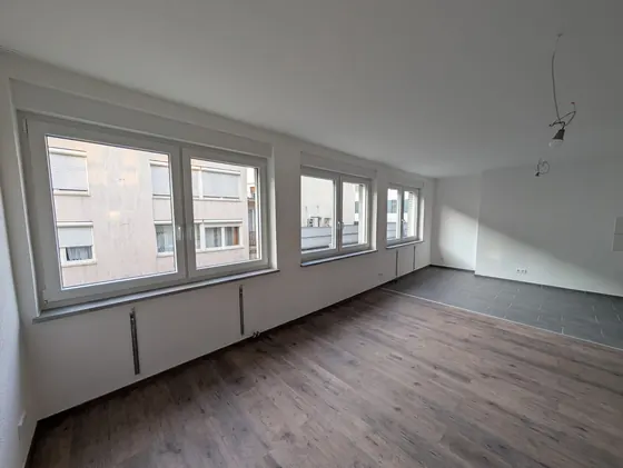 Innenausbau eines hellen Wohnraums mit neuen Bodenbelägen, großen Fenstern und vorbereiteten Deckenanschlüssen