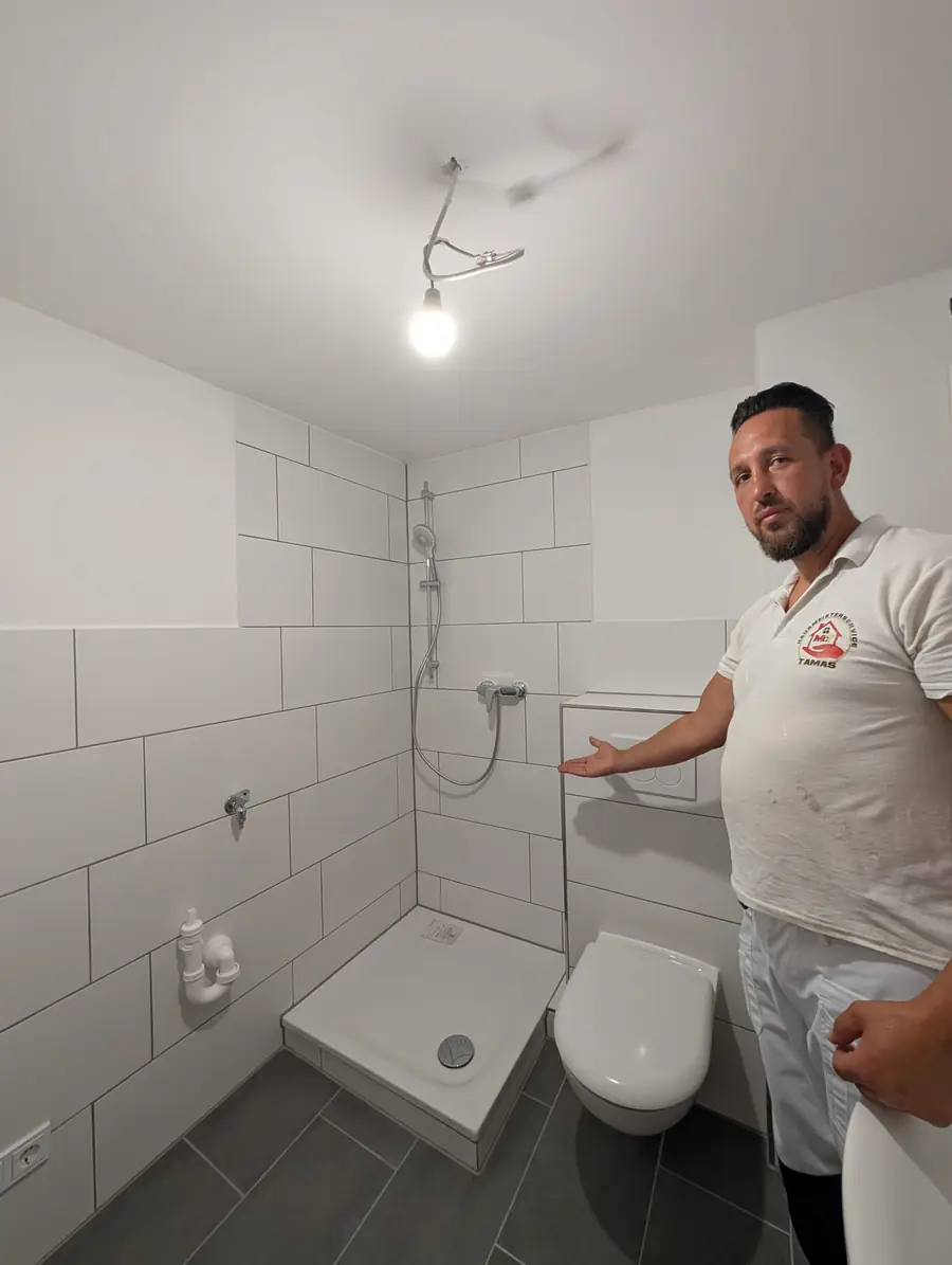 Modernisiertes Badezimmer mit Dusche, weißen Wandfliesen und dunklen Bodenfliesen.