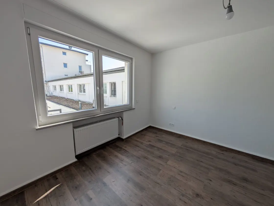 Helles Zimmer mit frisch verlegtem dunklem Laminatboden und Fensterbereich.