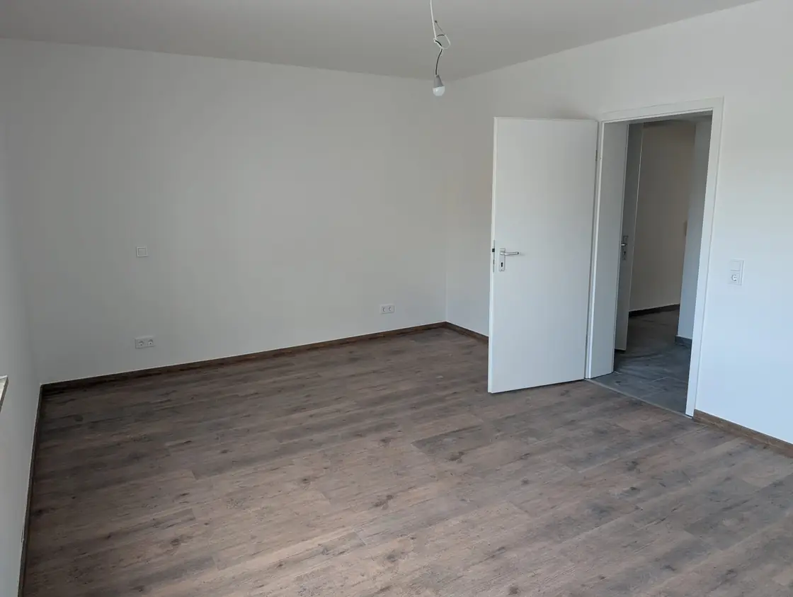 Renovierter Wohnraum mit dunklem Laminatboden, weißen Wänden und montierten Sockelleisten.