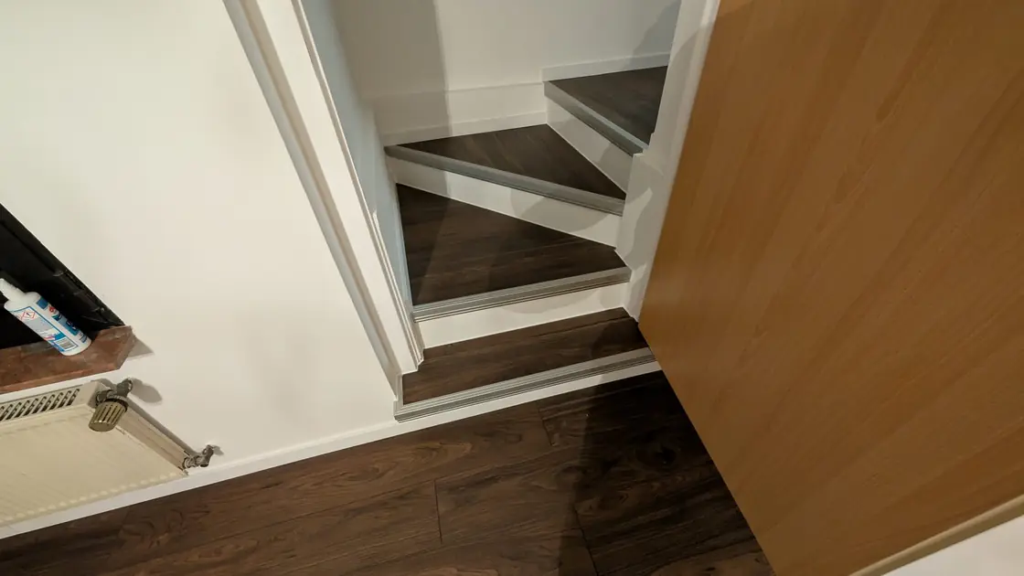 Treppenstufen und angrenzender Flur mit dunklem Holzdekor-Bodenbelag.