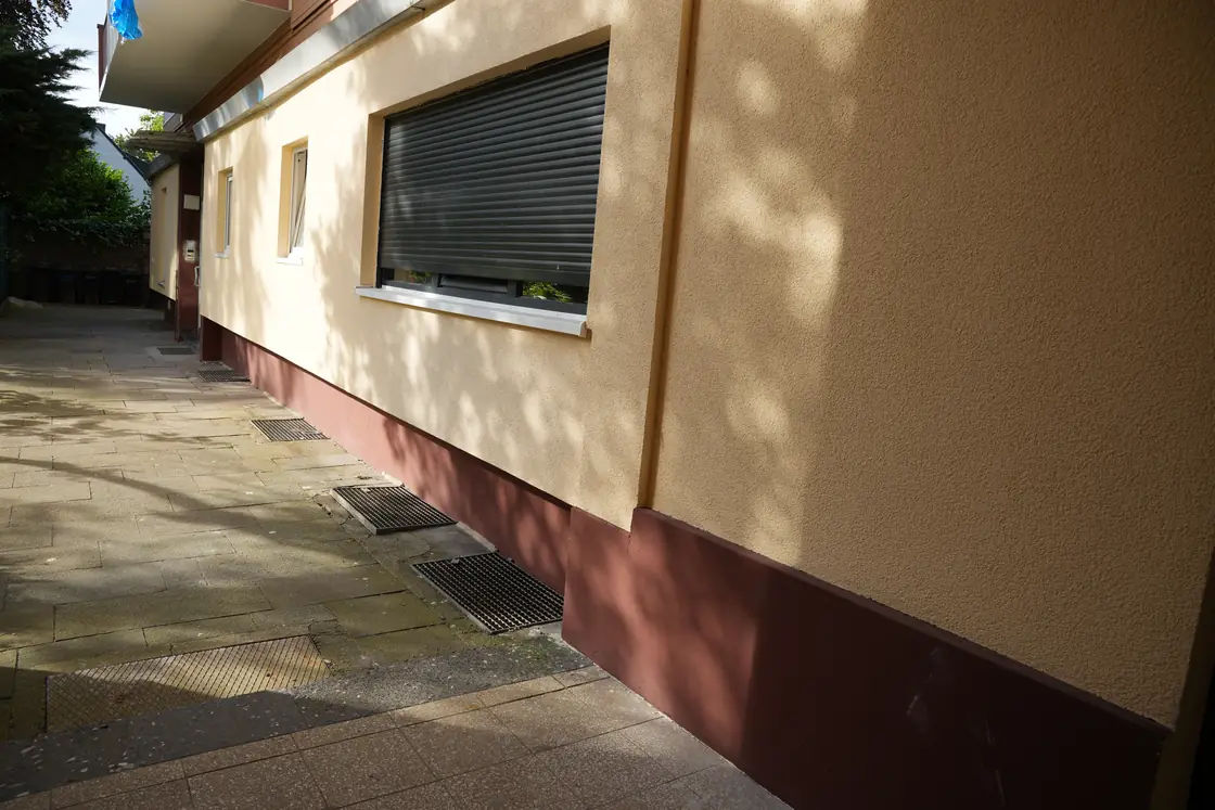 Hausfassade mit hellem Fassadenanstrich und dunkel abgesetztem Sockelbereich.