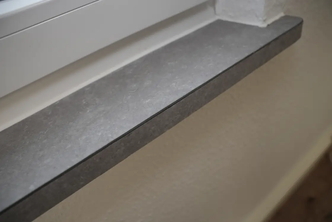 Nahaufnahme einer montierten grauen Fensterbank unter einem weißen Fensterrahmen.