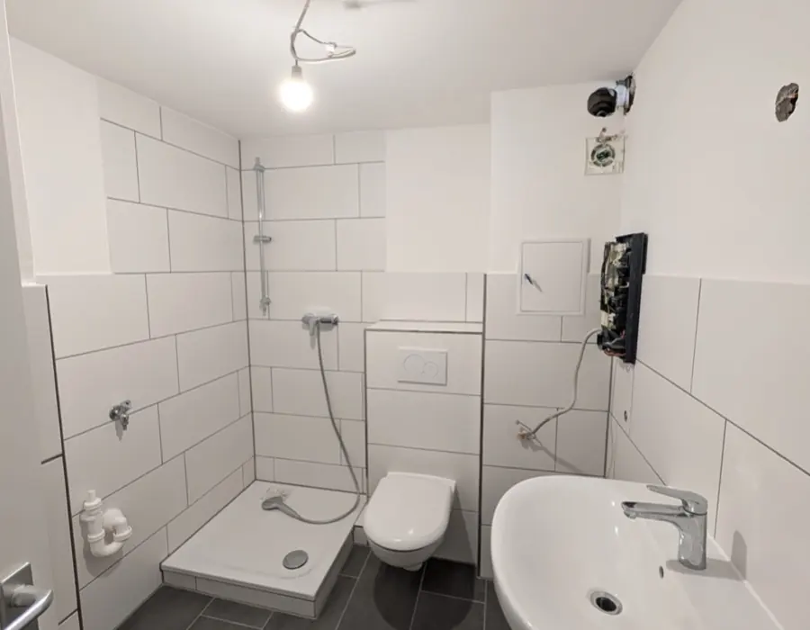Modernes Badezimmer mit großformatigen Fliesen, bodengleicher Dusche, WC und Waschbecken nach der Badsanierung.