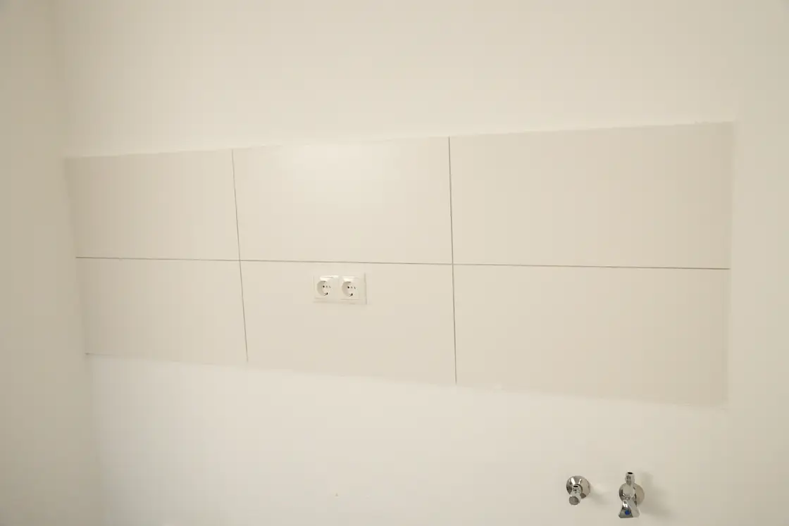 Küchenbereich mit sauber verlegten weißen Wandfliesen und vorbereiteten Anschlüssen.